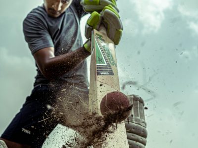A focused cricket player striking a ball with dramatic effect outdoors.